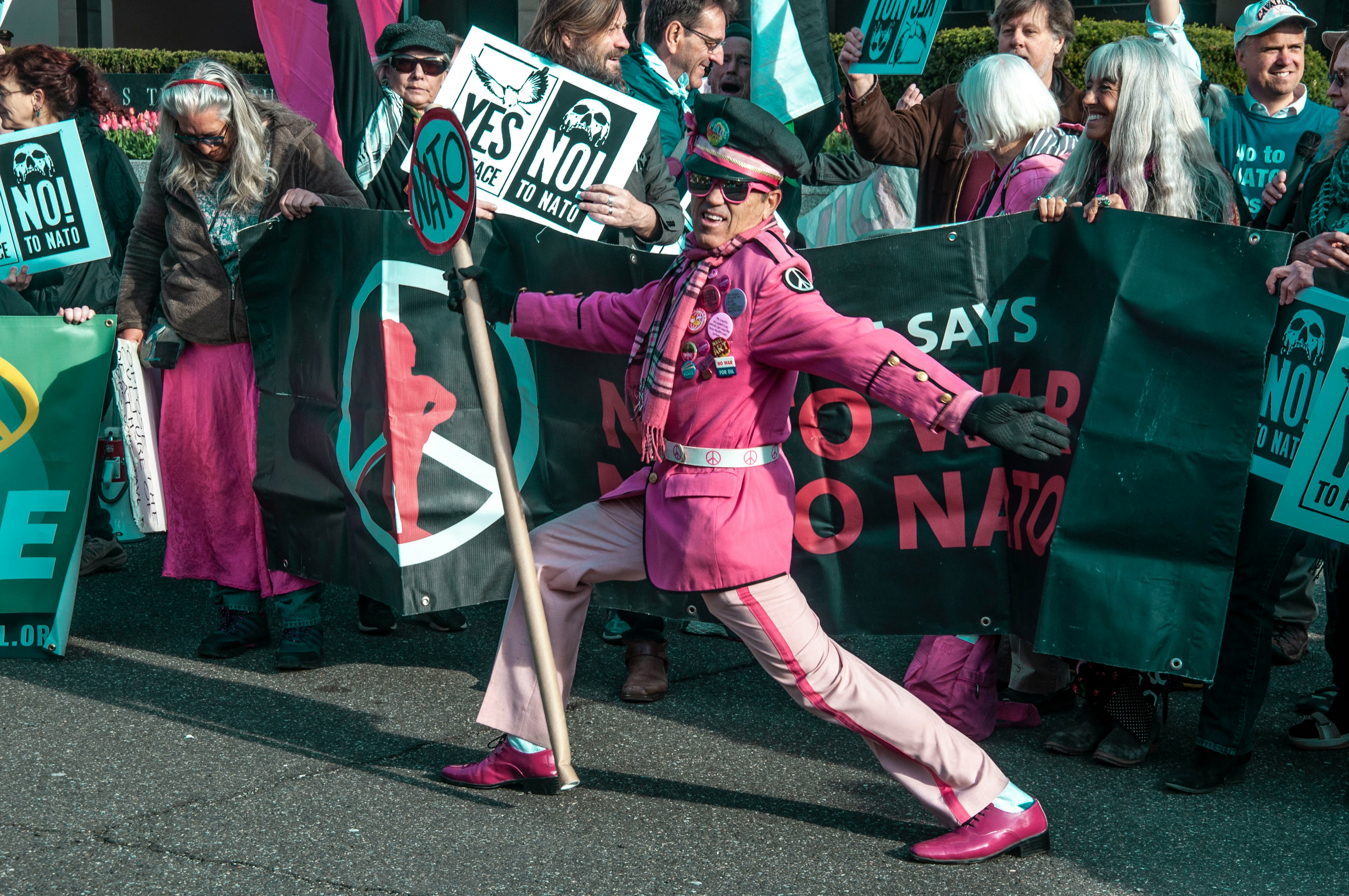 man in pink coat holding sign in front of card holding signs